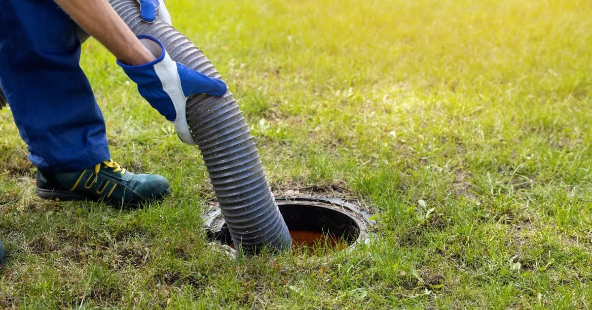 a person inserting a plumbing tube into the septic tank
