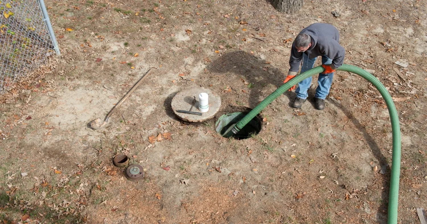 a man holding a green plumbing tube and inserting it into the septic tank