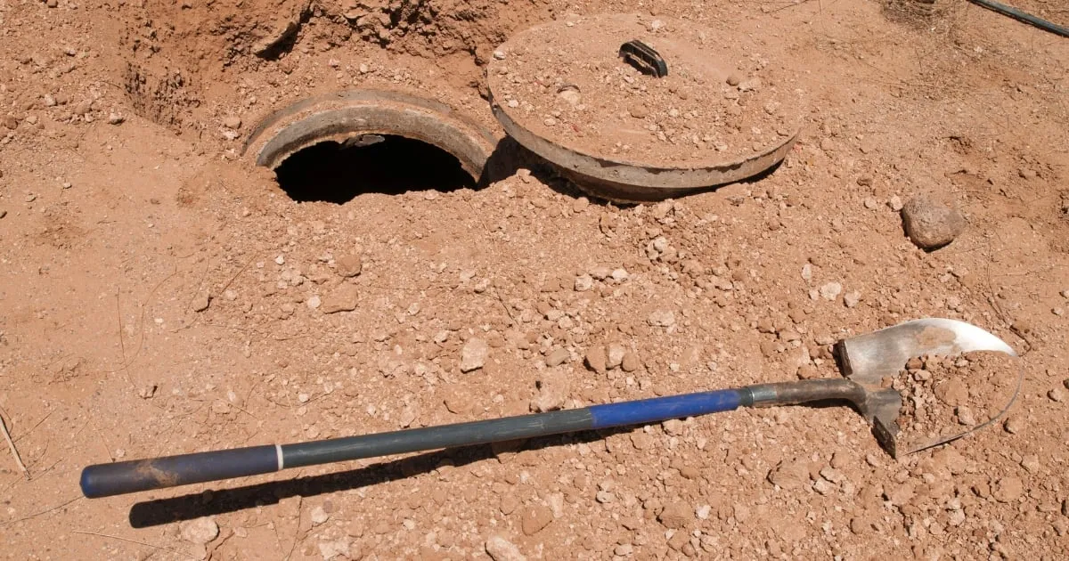 an open septic tank covered in soil and a shovel