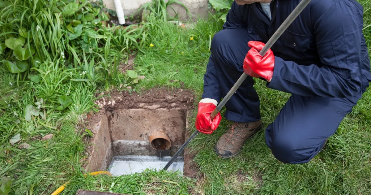 a man holding a metal stick and fixing the blocked drainage
