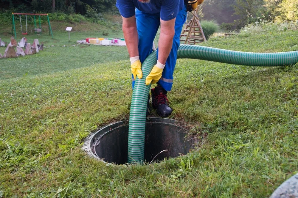Pump-out hose being fed into an open septic tank on a grassy Central Coast property