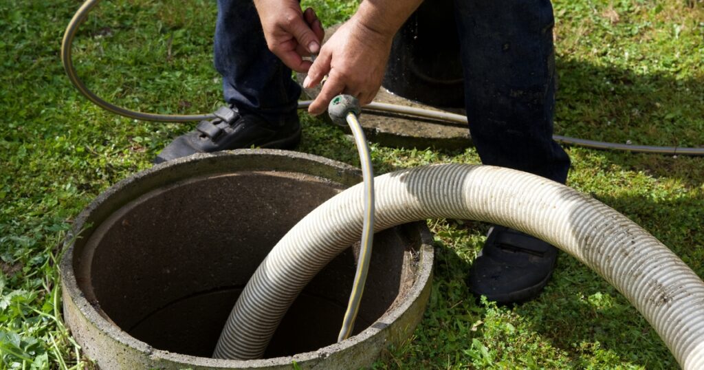 a hand inserting a hose into the septic tank system